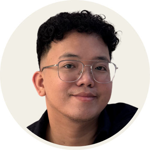 Professional headshot of a smiling man with short curly hair and glasses, wearing a dark shirt against a neutral background